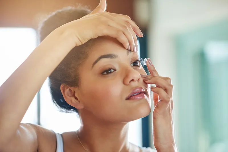 contact-lens-safety a woman in her bathroom putting in a contact lens